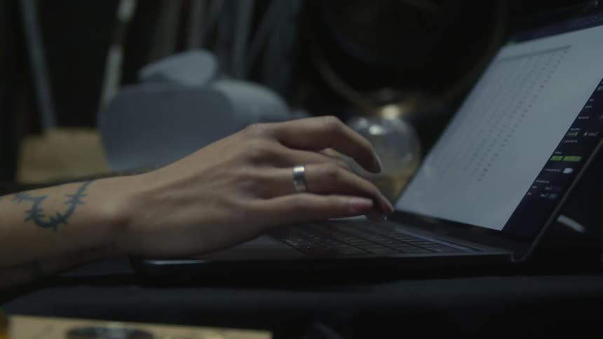 Woman with tattoos and ring works on laptop in room