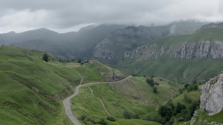 Dense fog covers mountains as road and tracks meander along green slopes of Cantabria