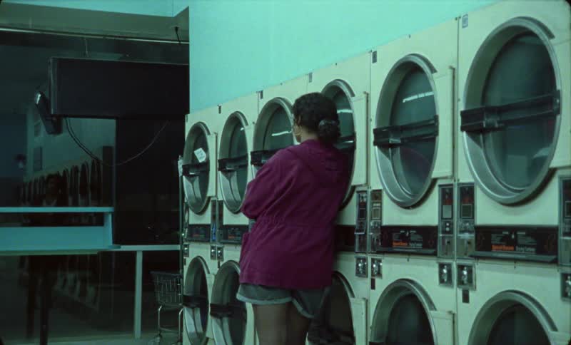 Young woman reclines on a washing machine inside a laundromat at night