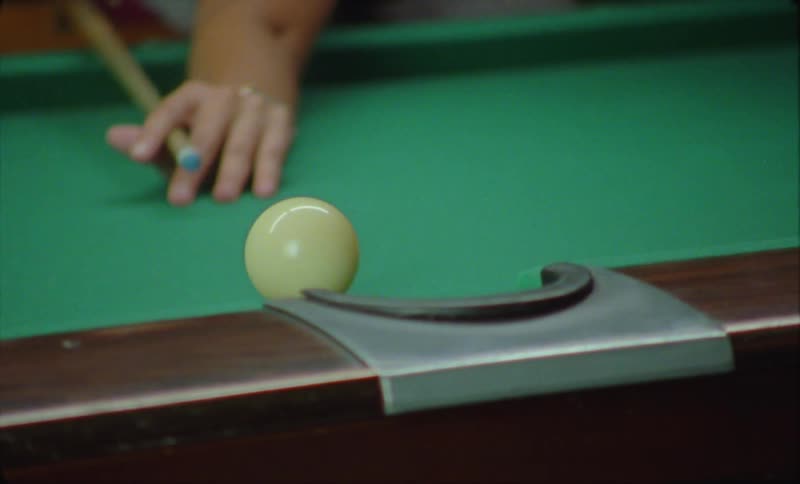 Close up of a person playing billiard using a cue to pocket the eight ball