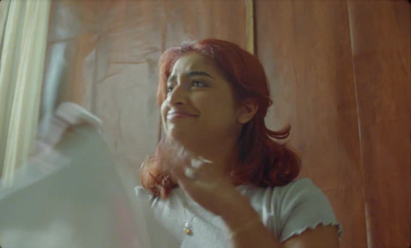 A young hispanic woman is folding clothes inside of her house