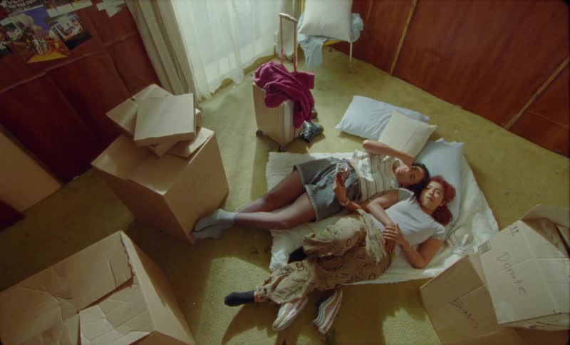 Two young woman are lying on a blanket on the floor talking surrounded by boxes as they are in the process of moving