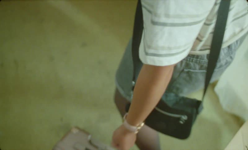 Woman standing in her bedroom checks her wristwatch before picking up luggage for a travel