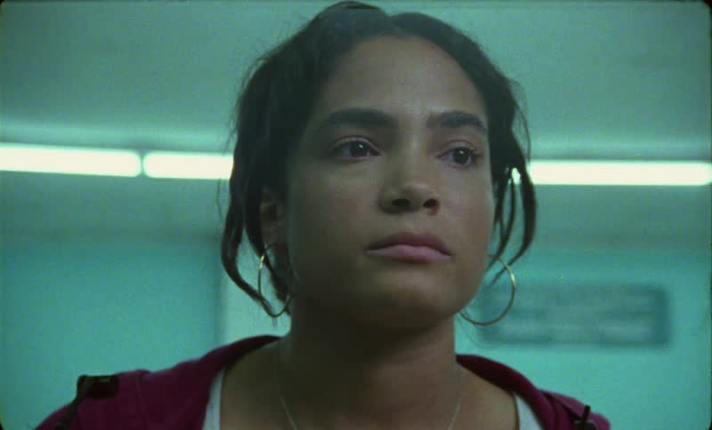 Teary eyed woman with wavy hair hoop earrings and red top looks around