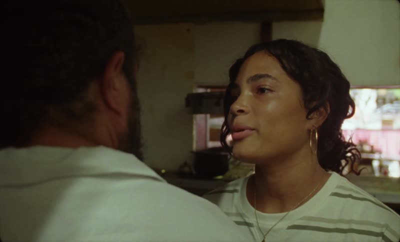 A woman in a restaurant kitchen takes off her apron and kisses the cook as she leaves