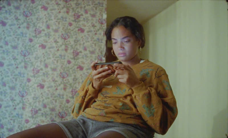 A girl is sitting in a room looking upset as she reads on her cellphone