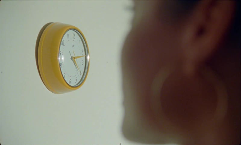 A woman in a room stops to look at a clock before walking away