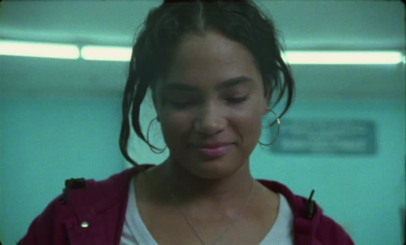 Woman with wavy hair hoop earrings and red full zip hoodie looks down and smiles slightly