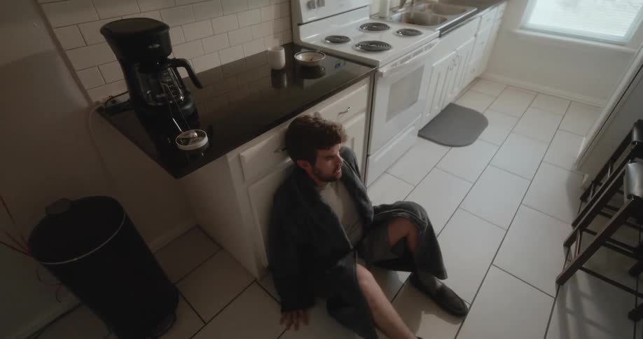 Person sits down on the floor next to kitchen counter to hide