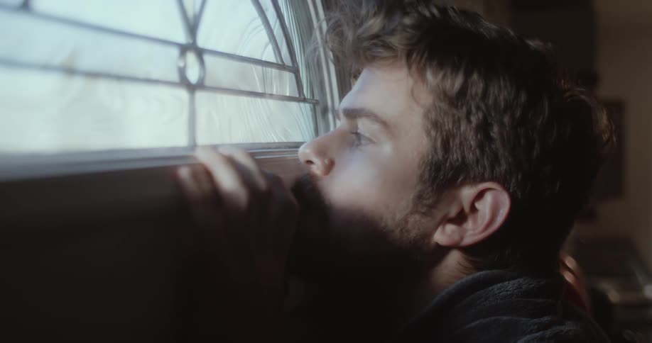 A man walks up to a front door and looks out the window