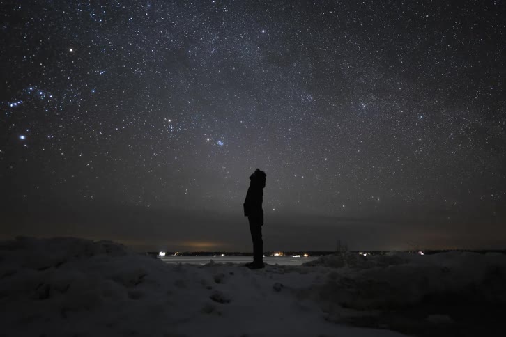 The silhouette of a person standing on a ridge with head back gazing at the starry night sky