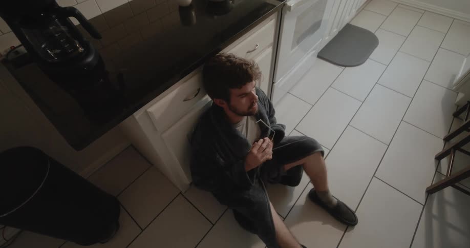 There is a man sitting on the floor inside of his home and looks scared