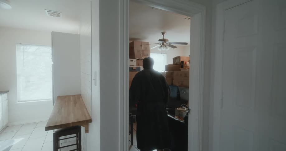 A white man is walking inside of his house in the middle of the day