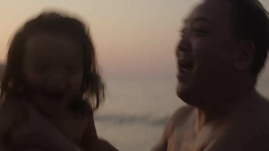 A man lifts and dips his child in the ocean as they both laugh with joy