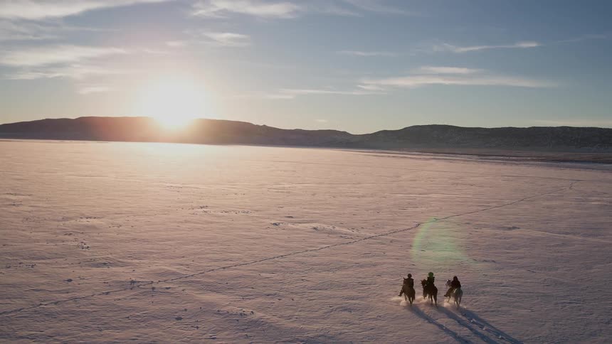 Three people are riding horses across a snow covered field