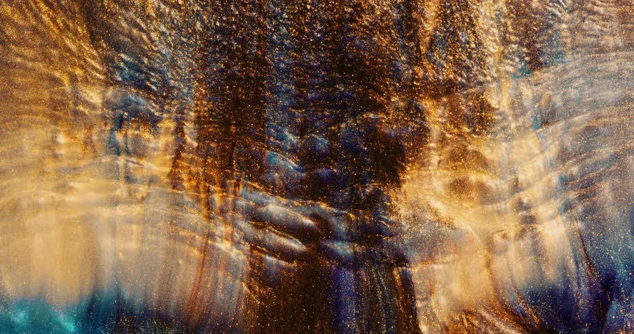 An organic liquid substance is rippling and as it moves upward it glitters and colors slowly blend together