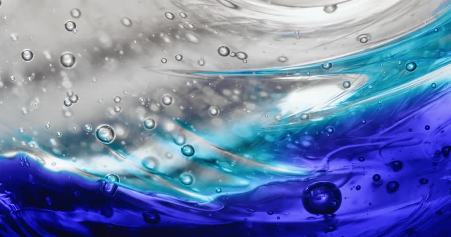 Bubble spheres reflect light and colors as they float in a moving mixture of light blue and electric blue substance on white