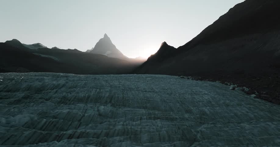 The sun shining from behind mountain peaks onto glacier ice and ridges
