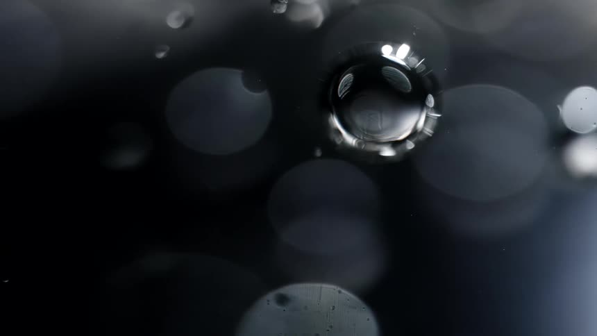 Extreme close up of air bubbles and specs of dust floating on the surface of clear water
