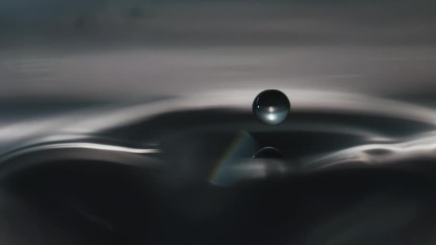 Droplets fall into water and ripple and splash as they reflect the light