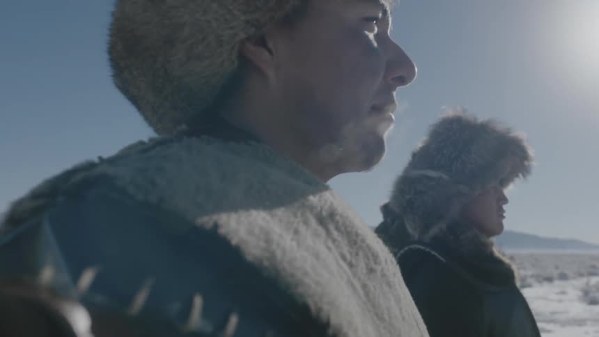Two men stand on a snow field on a windy day