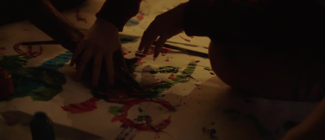Woman guides mans hand in finger painting on paper as they sit on the floor opposite each other