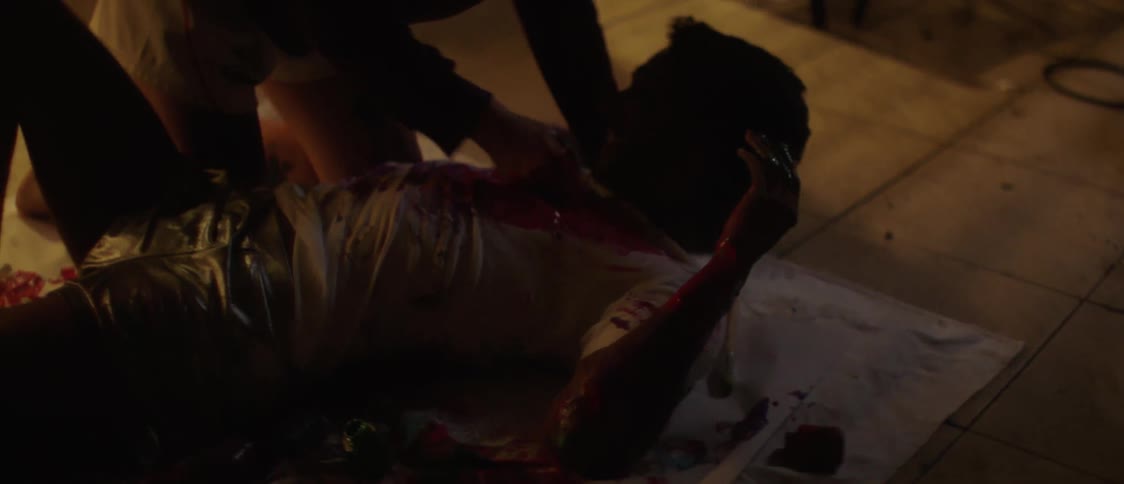 Woman smears paint on mans chest after pressing his arm to the cloth he is lying on