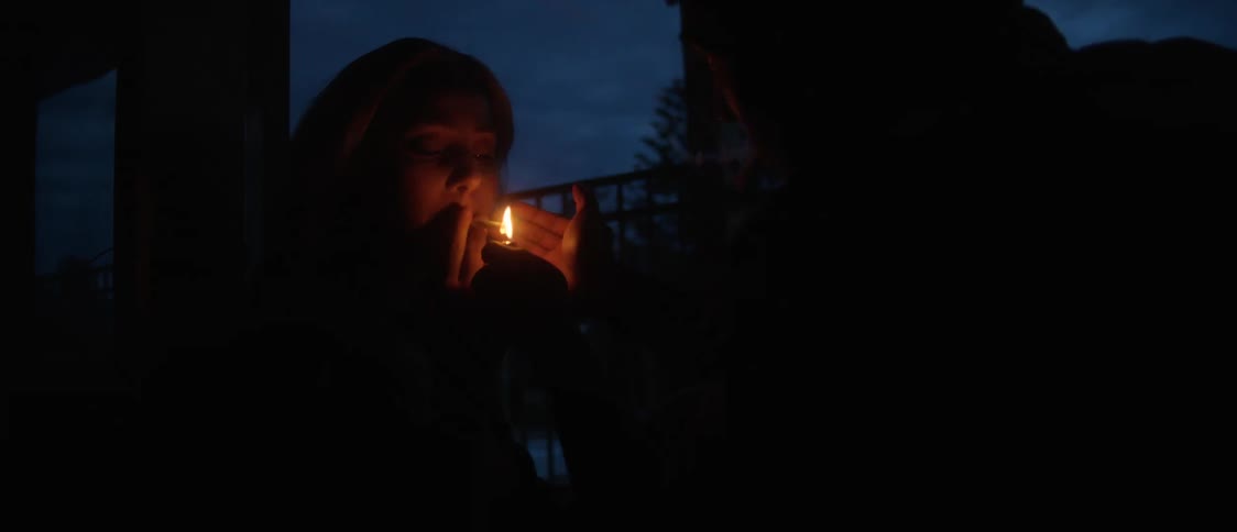 Couple sitting at table lights up cigarette at night outdoors