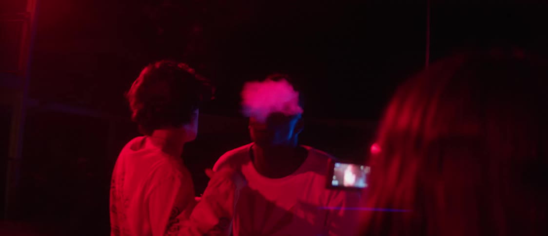 Woman with wavy hair films men drinking dancing and smoking in red light in the street