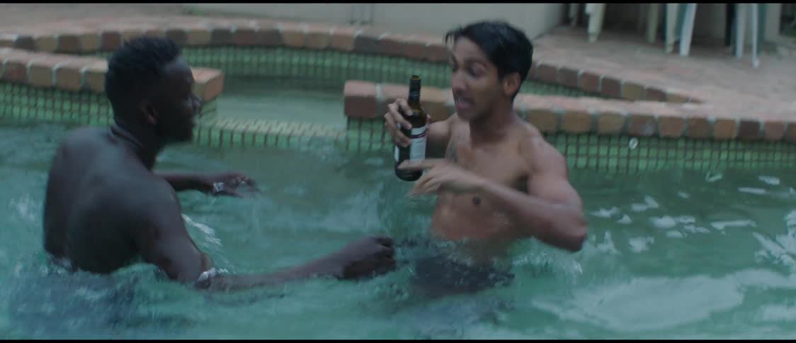 Two men are in a swimming pool and one man is holding a wine bottle and the other man is trying to take it from him