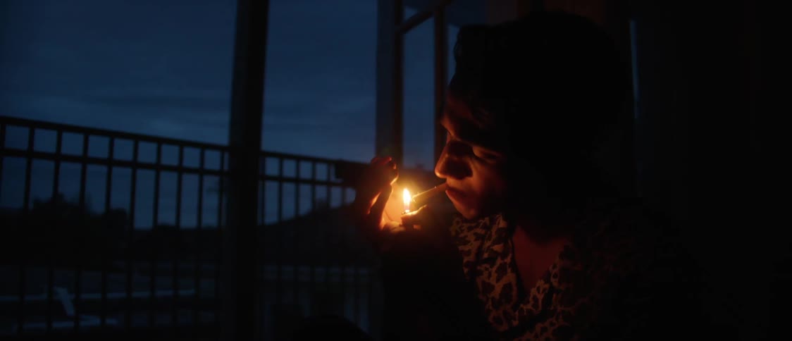 Silhouette of a young man lighting a cigarette while sitting in the dark porch at evening