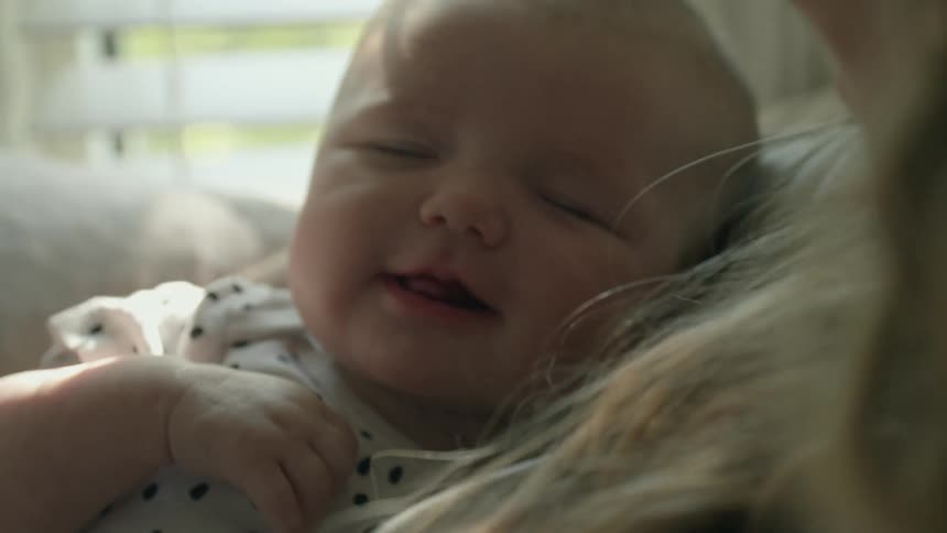 Mother smiles while reclining near window with baby