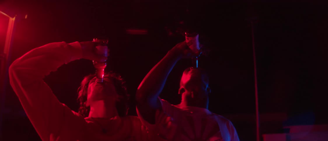 Two young men standing next to each other outside and they tip their beer bottles and drink