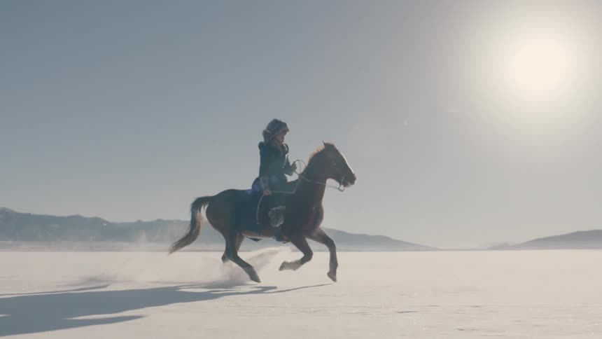 A lone horseman riding a galloping horse across a snowy landscape