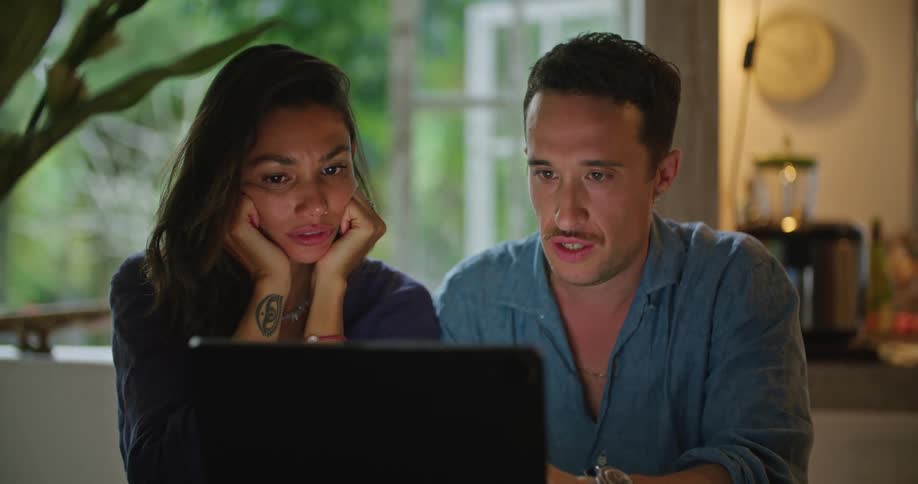 A man and woman sitting next to each other while looking at a laptop screen