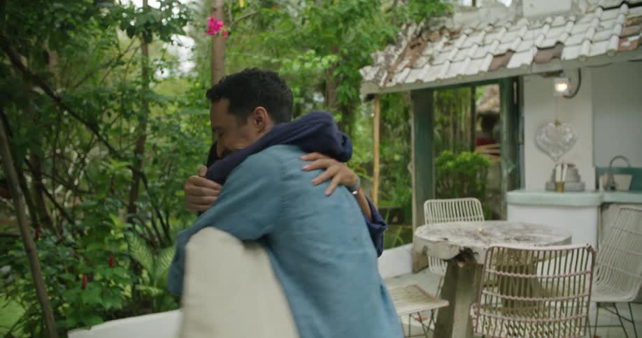 Man greets woman with a hug as she arrives at patio behind house