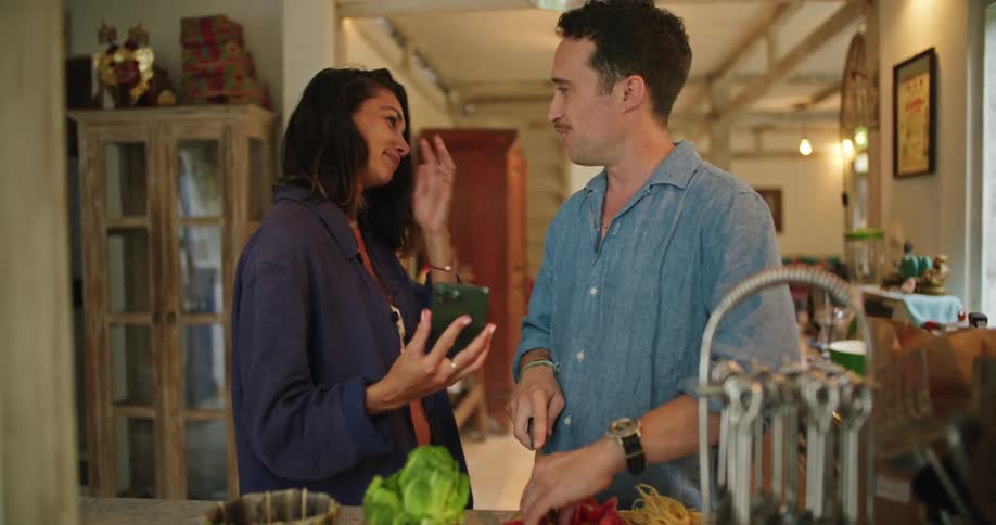 A couple talk and look at a phone as the man cuts food