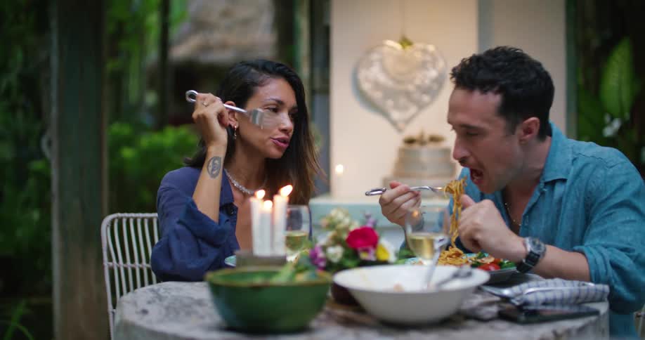 Young couple eating a hearty meal at candle light on a table in the backyard