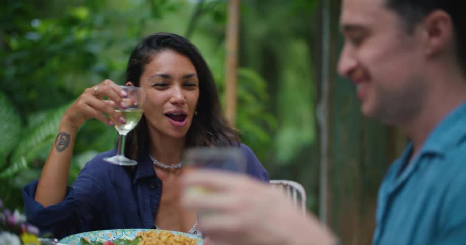 A man and a woman are sitting down at a table talking and they raise their wine glasses and toast a drink