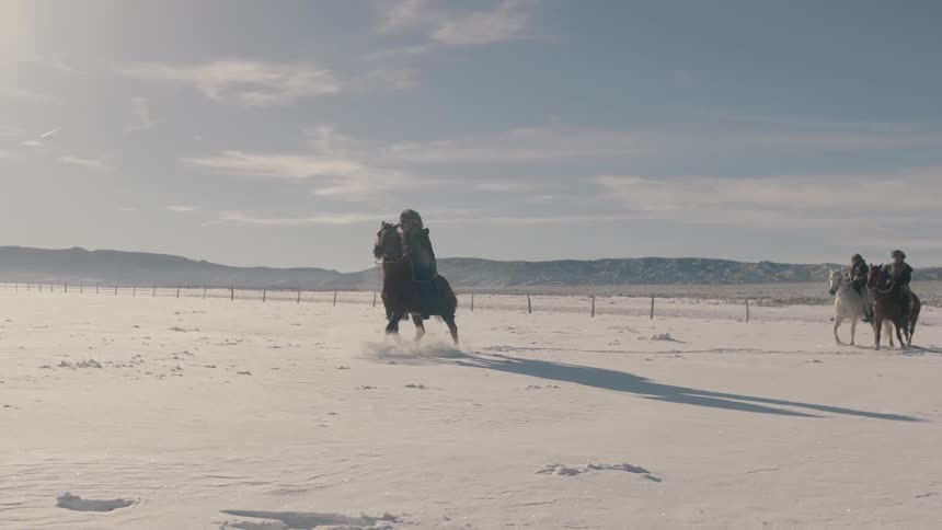 People riding horses across a snow covered pasture