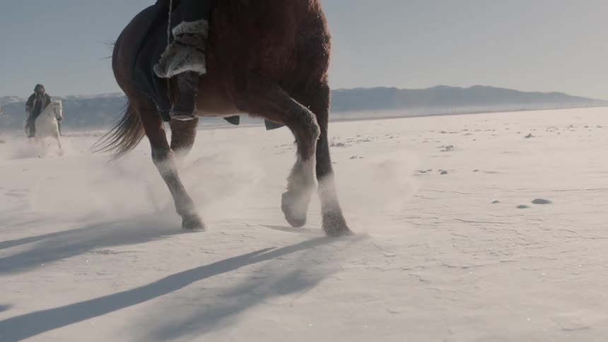 Two men riding horses and snowy ground with mountains in the background