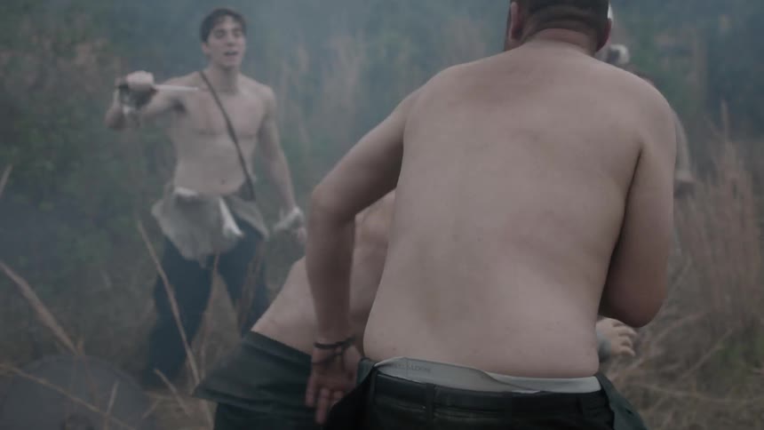Men in medieval style outfits watching two other men fight in a field