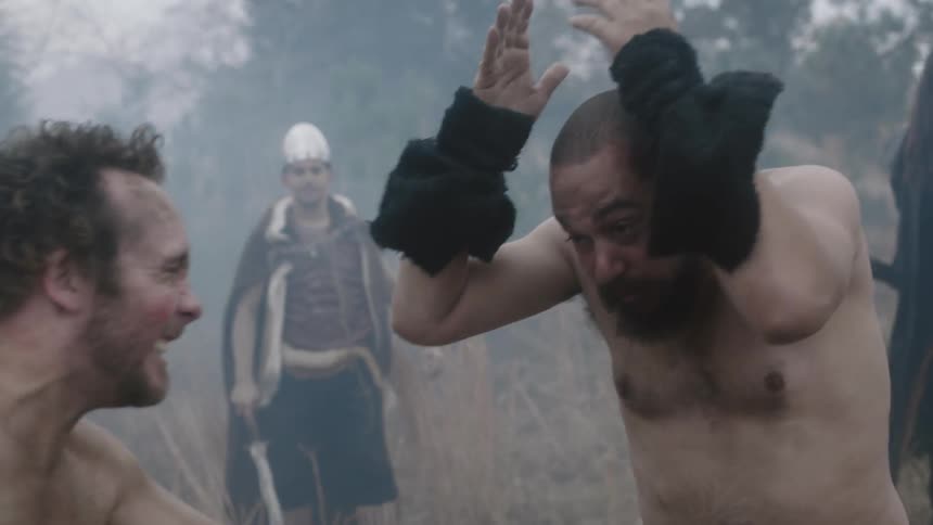 Two men fight while people form a circle around them and egg them on