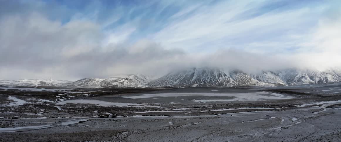 Snow dusted mountain range with cloud cover next to lava fields