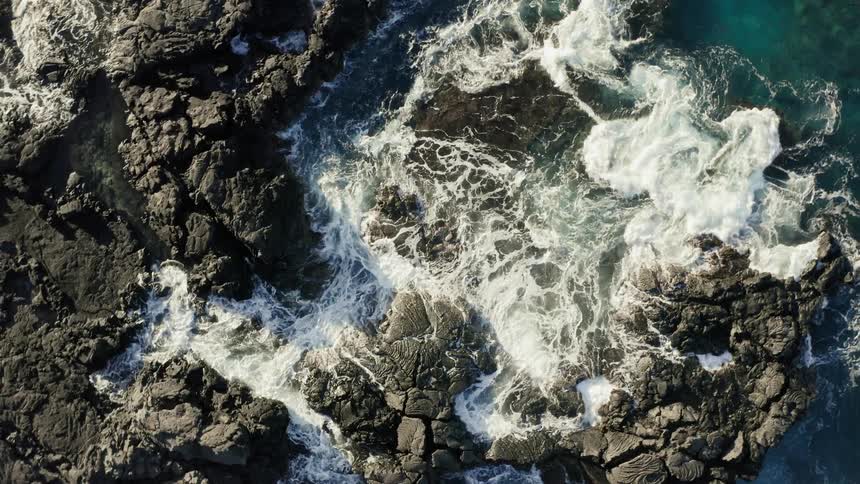 An aerial view of ocean waves crashing ashore a rocky beach
