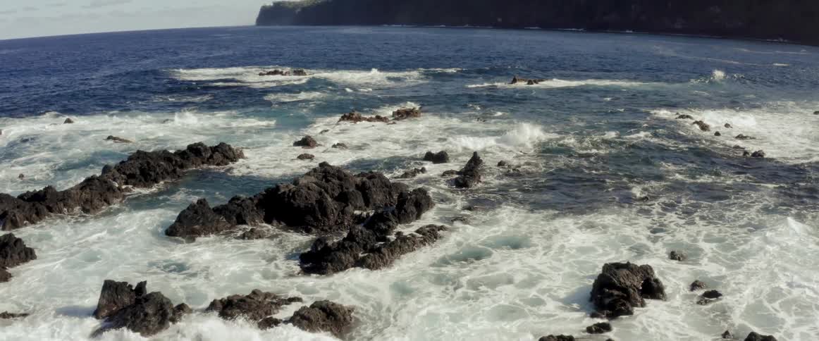 Ocean waves break splash and foam against rocks near shore