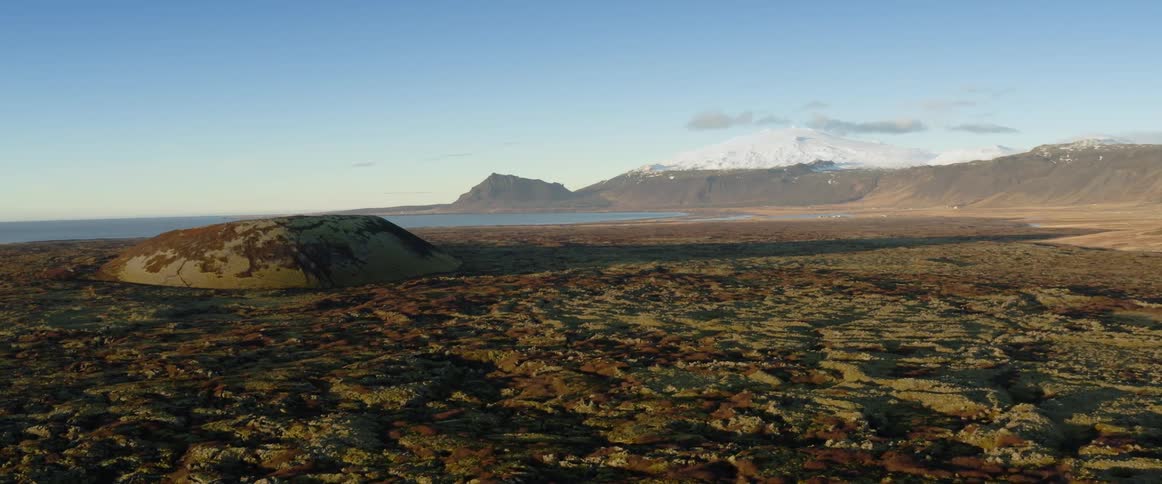A snow capped mountain and ridge along the water with rocky barren landscape