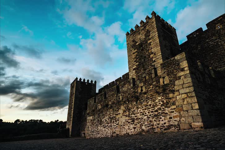 The sun shines on an old castle as clouds move in the sky and it gets darker outside
