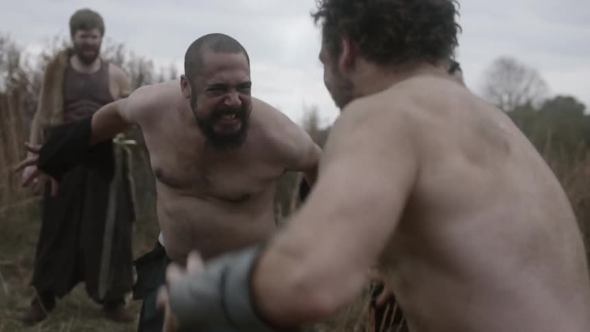 Two men fight as a group of other men stand in a circle around them