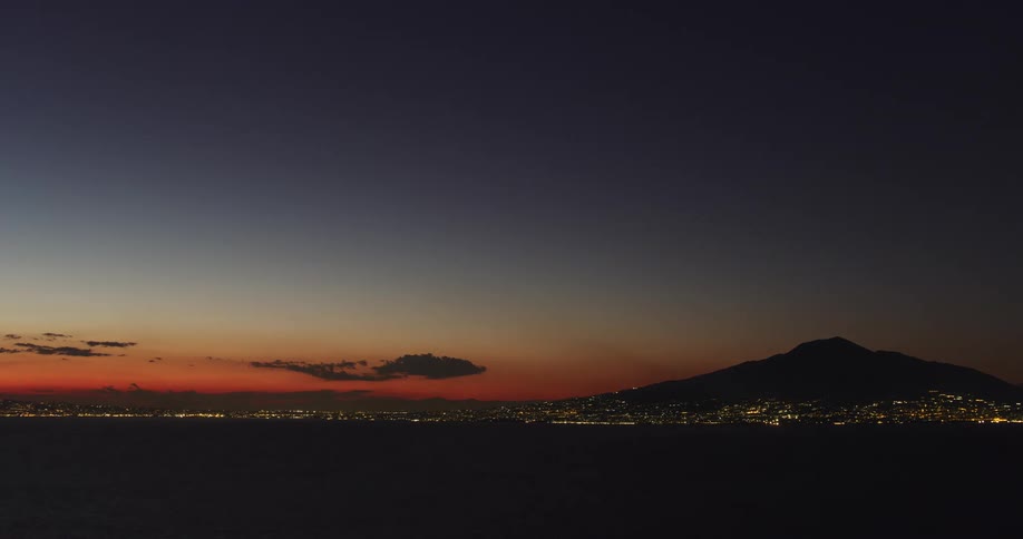 The sun setting in the sky above the silhouette of a mountain with shimmering city lights below